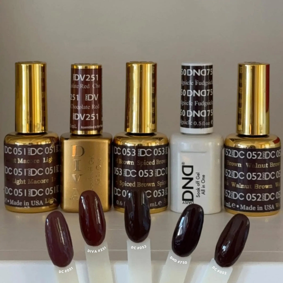 DND gel polish bottles with nail tip swatches labeled DC #051 Light Macore, DIVA #251 Chocolate Red, DC #053 Spiced Brown, DND #750 Fudgsicle, and DC #052 Walnut Brown
