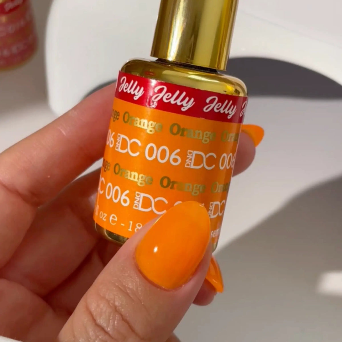 Hand with almond nails in orange jelly polish holding a DC Jelly #006 Orange bottle