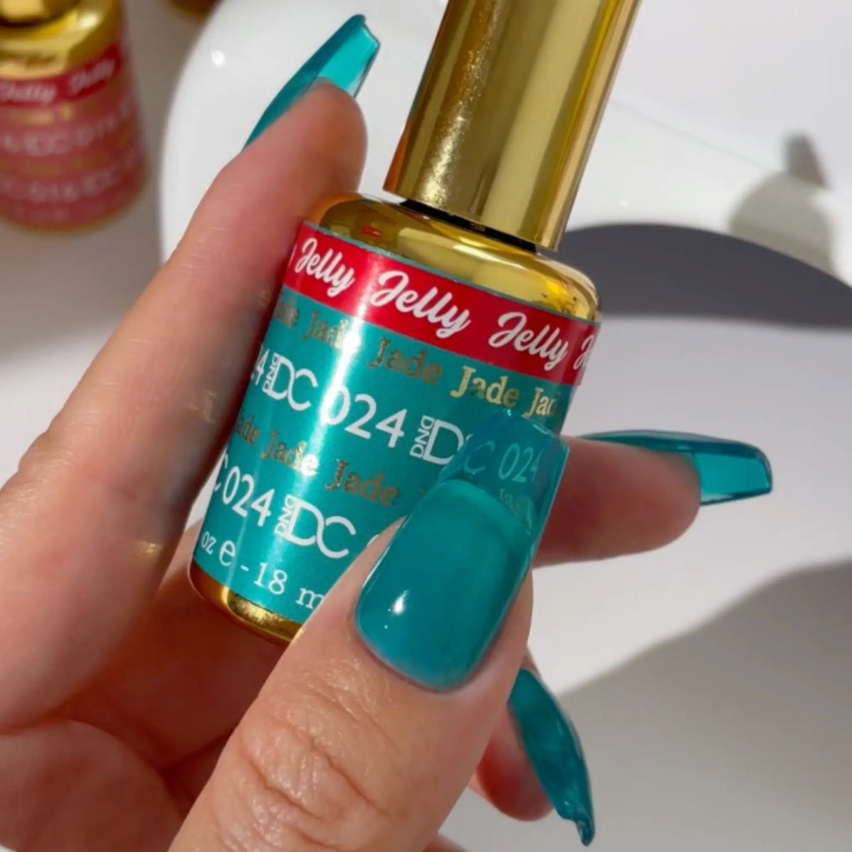 Hand with long stiletto nails in turquoise green-blue jelly polish holding a DC Jelly #024 Jade bottle