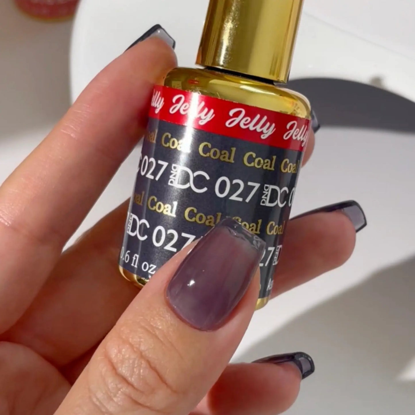 Close-up of a square nail in dark smoky grey jelly polish beside a DC Jelly #027 Coal bottle