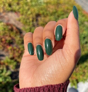 Hand with dark green nails, DC #326 Nightrider gel polish, outdoor background
