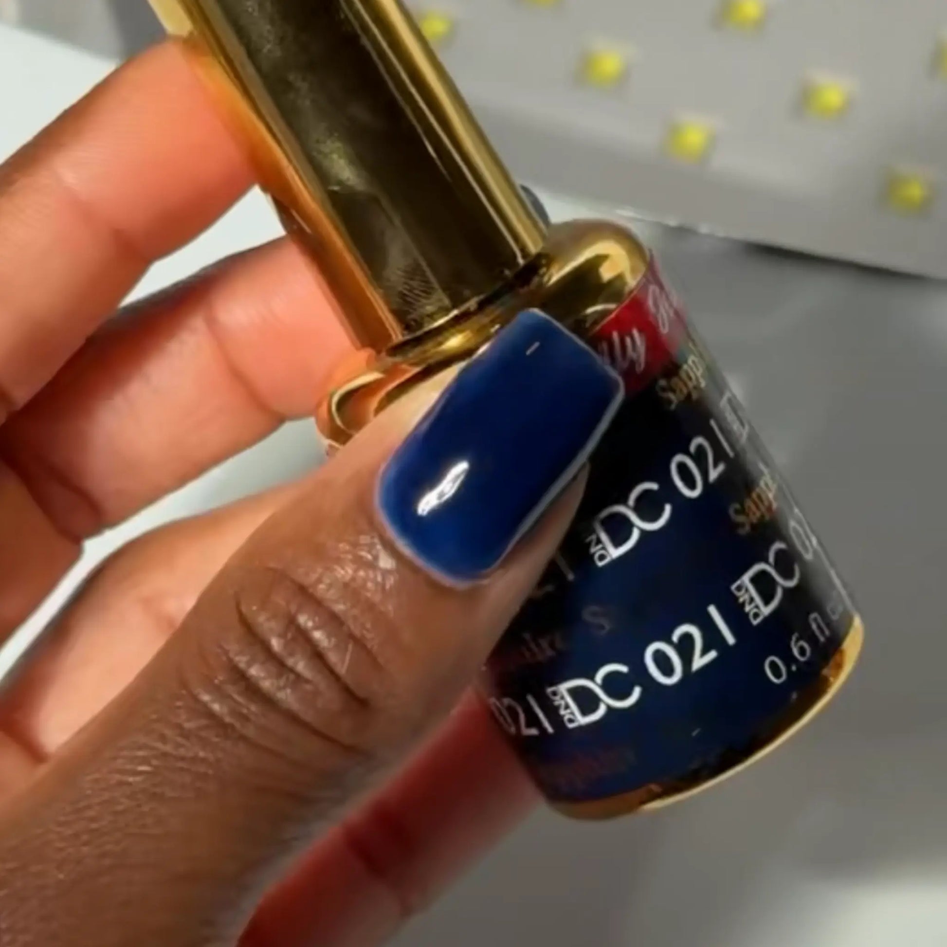 Hand with navy blue manicured nail holding a bottle of DC #021 gel nail polish