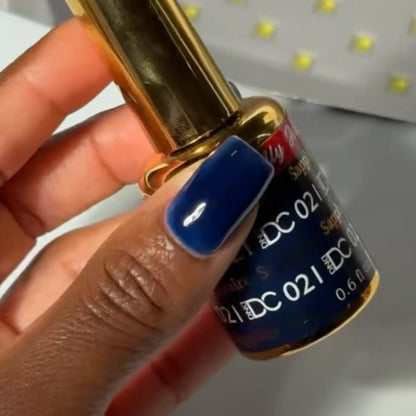 Hand with navy blue manicured nail holding a bottle of DC #021 gel nail polish