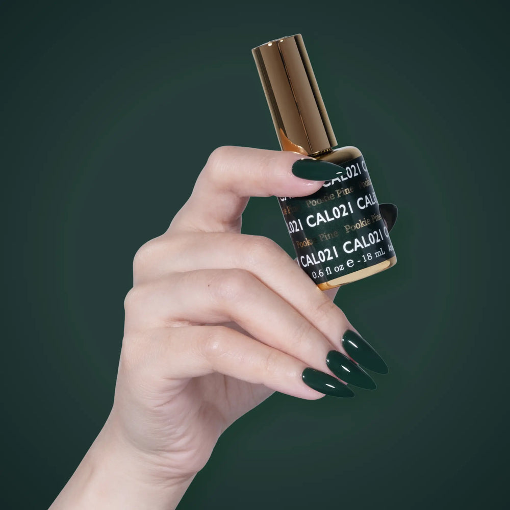 Hand with dark green nails holding a DND CAL021 Pookie Pine bottle against a dark green background