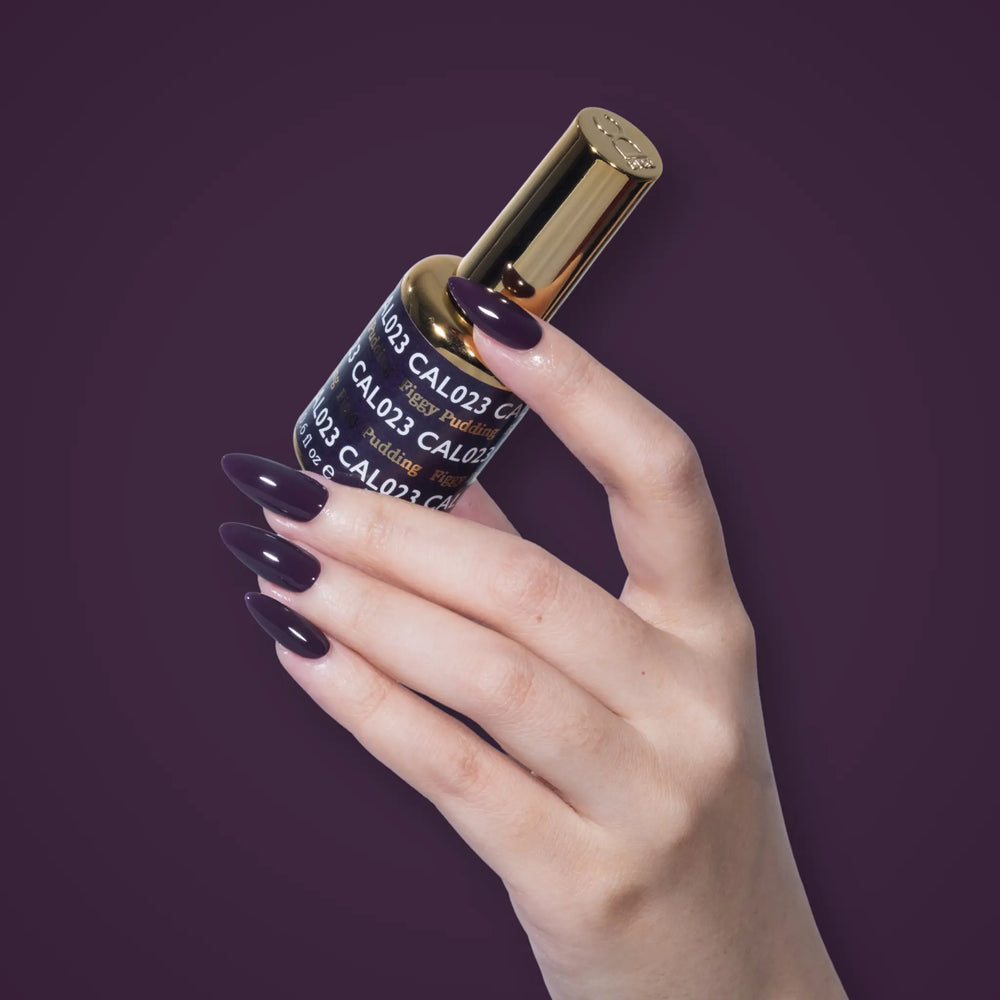 Hand with deep plum nails holding a DND CAL023 Figgy Pudding bottle against a purple background