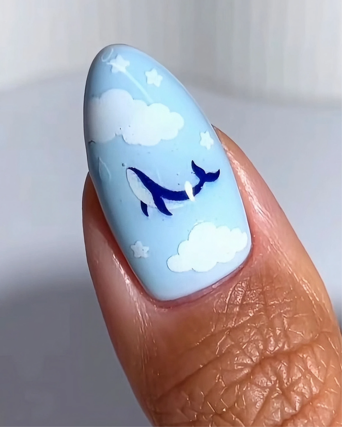 Close-up of a nail in pale blue with cloud and whale nail art stickers