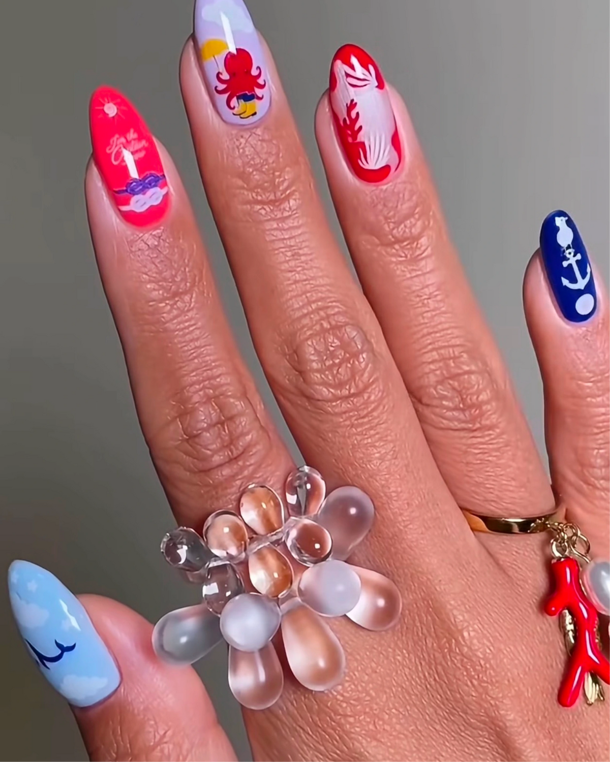 Hand with red, blue and pale blue nails wearing nautical nail art stickers