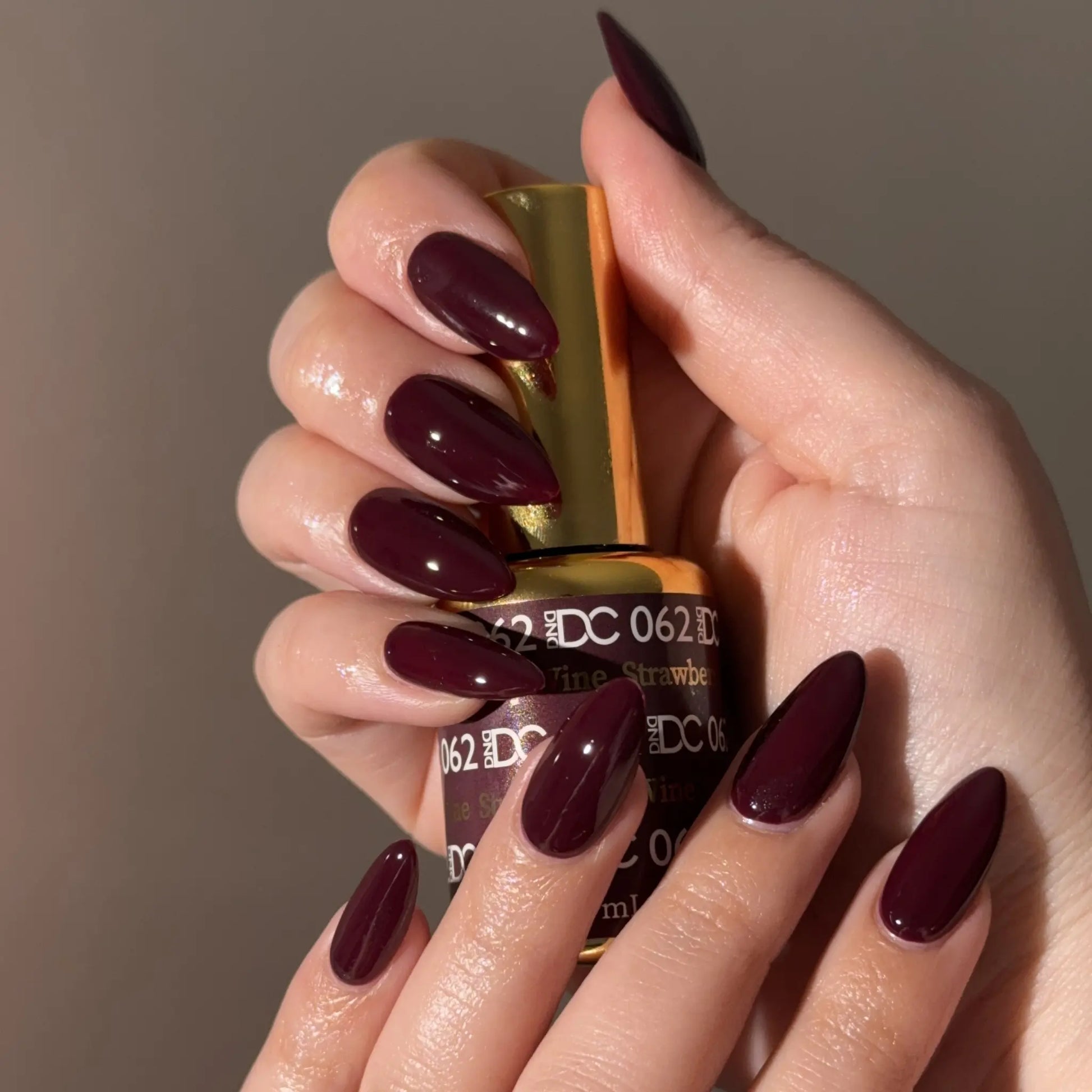 Hand with red wine nail polish holding a bottle of DC 062 nail polish.