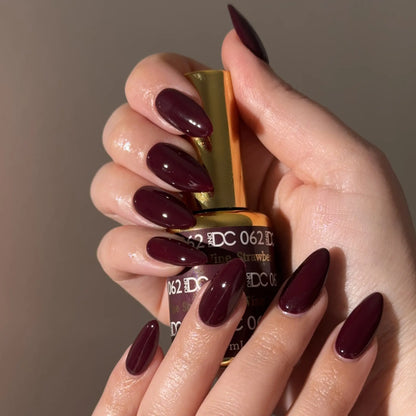 Hand with red wine nail polish holding a bottle of DC 062 nail polish.