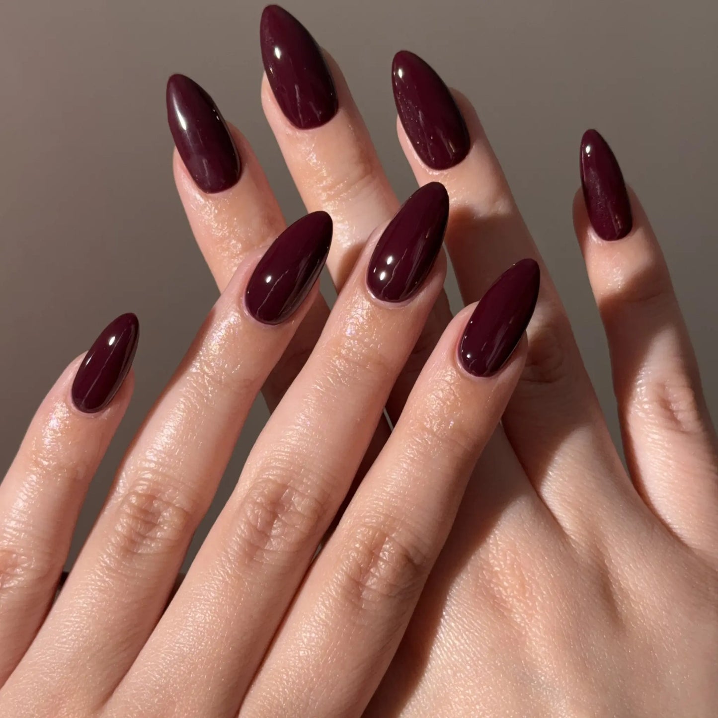 Close-up of hands with dark red nail polish on a neutral background