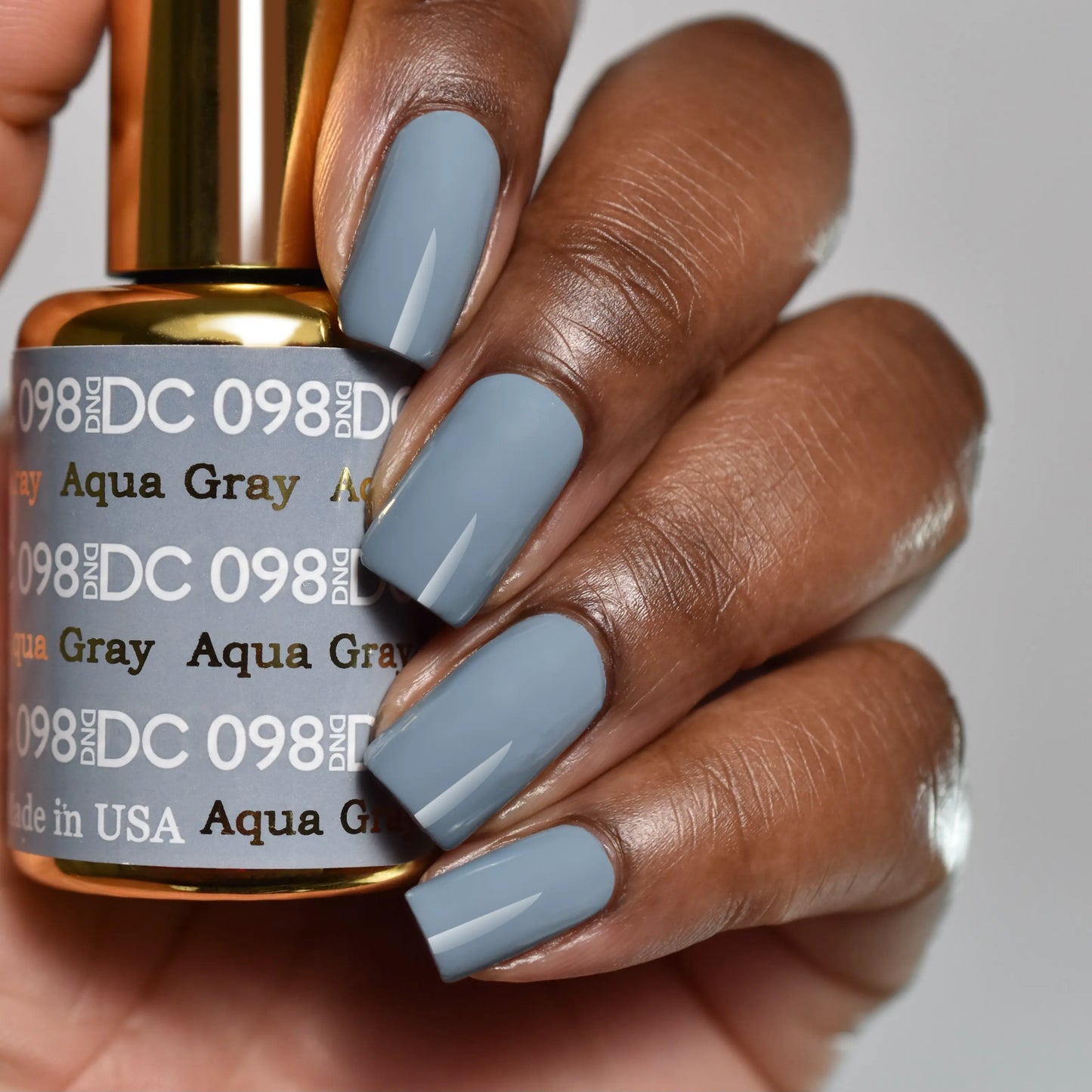 Close-up of hand with manicured nails in DC Aqua Gray #098 gel nail polish, steel blue cool slate grey, holding matching bottle