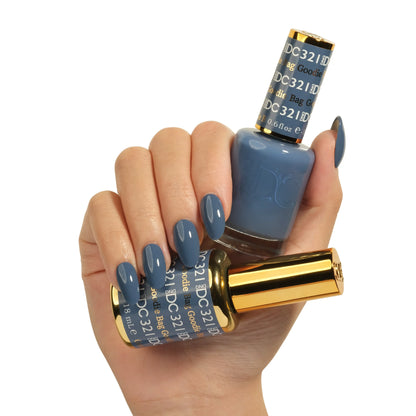 Hand holding two bottles of DC Goodie Bag #231 gel nail polish, dusty denim blue, with matching manicured nails