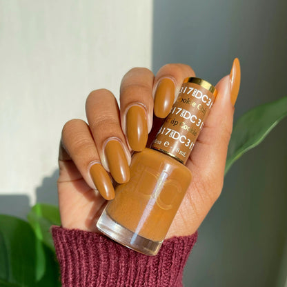 Hand with warm caramel brown manicured nails holding a bottle of DC Cookie Chip #317 gel nail polish
