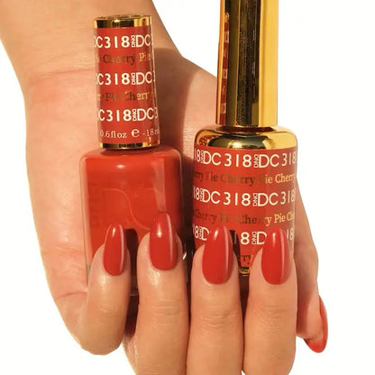 Hand holding two bottles of DC Cherry Pie #318 gel nail polish, with nails painted in the matching glossy warm autumn red