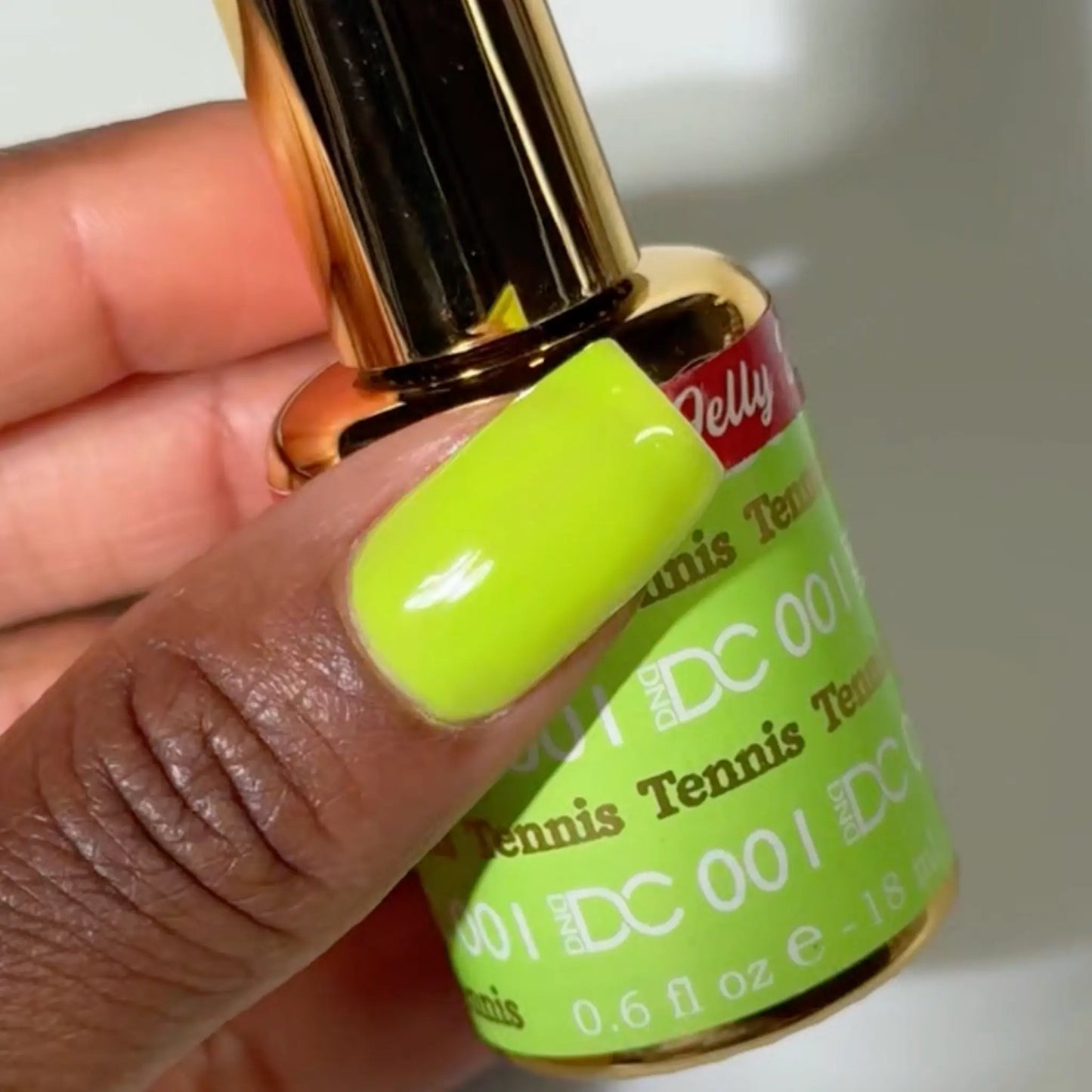 Close-up of a fingernail painted with DC Jelly Tennis fluorescent green-yellow jelly nail polish, next to a bottle of DND nail polish