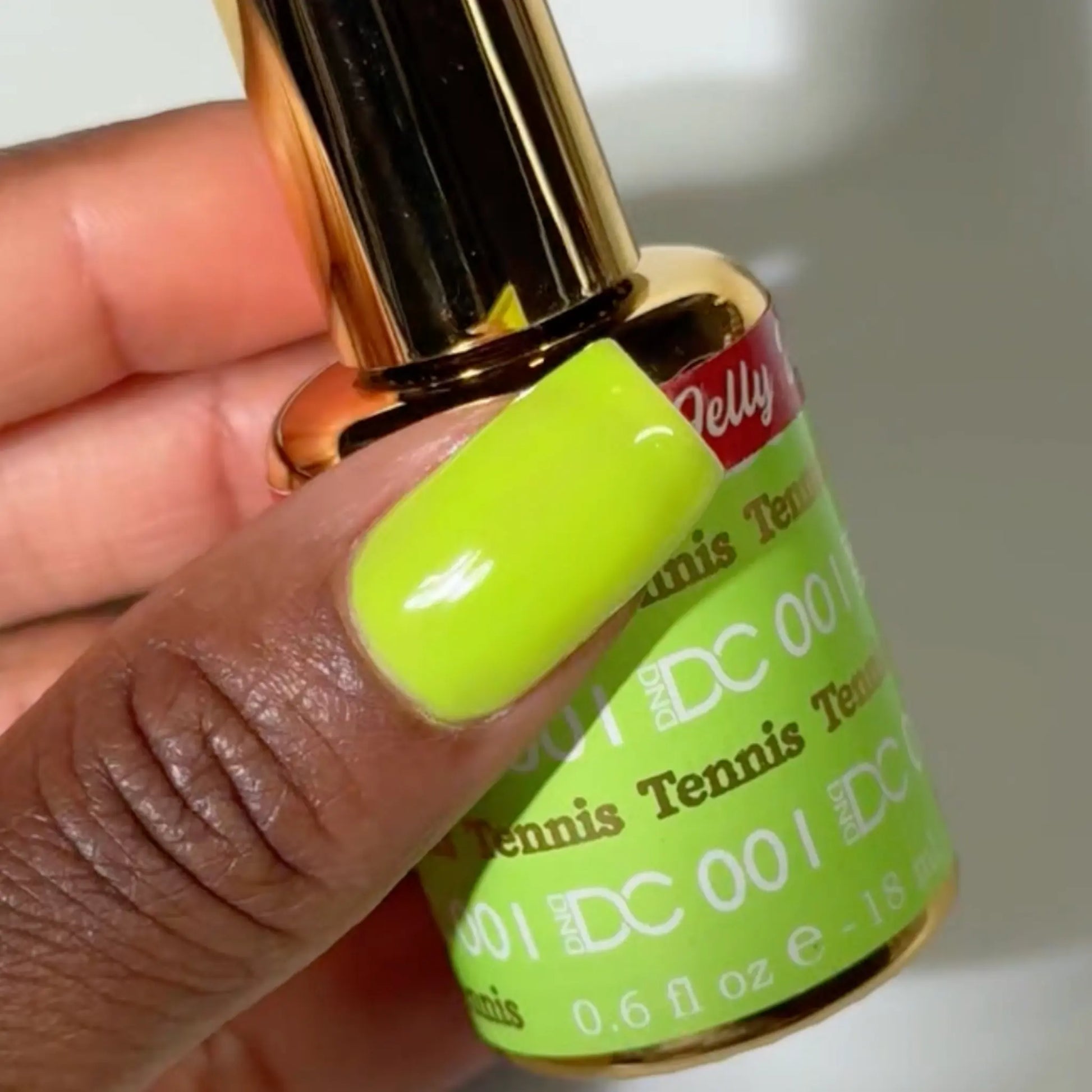 Close-up of a fingernail painted with DC Jelly Tennis fluorescent green-yellow jelly nail polish, next to a bottle of DND nail polish
