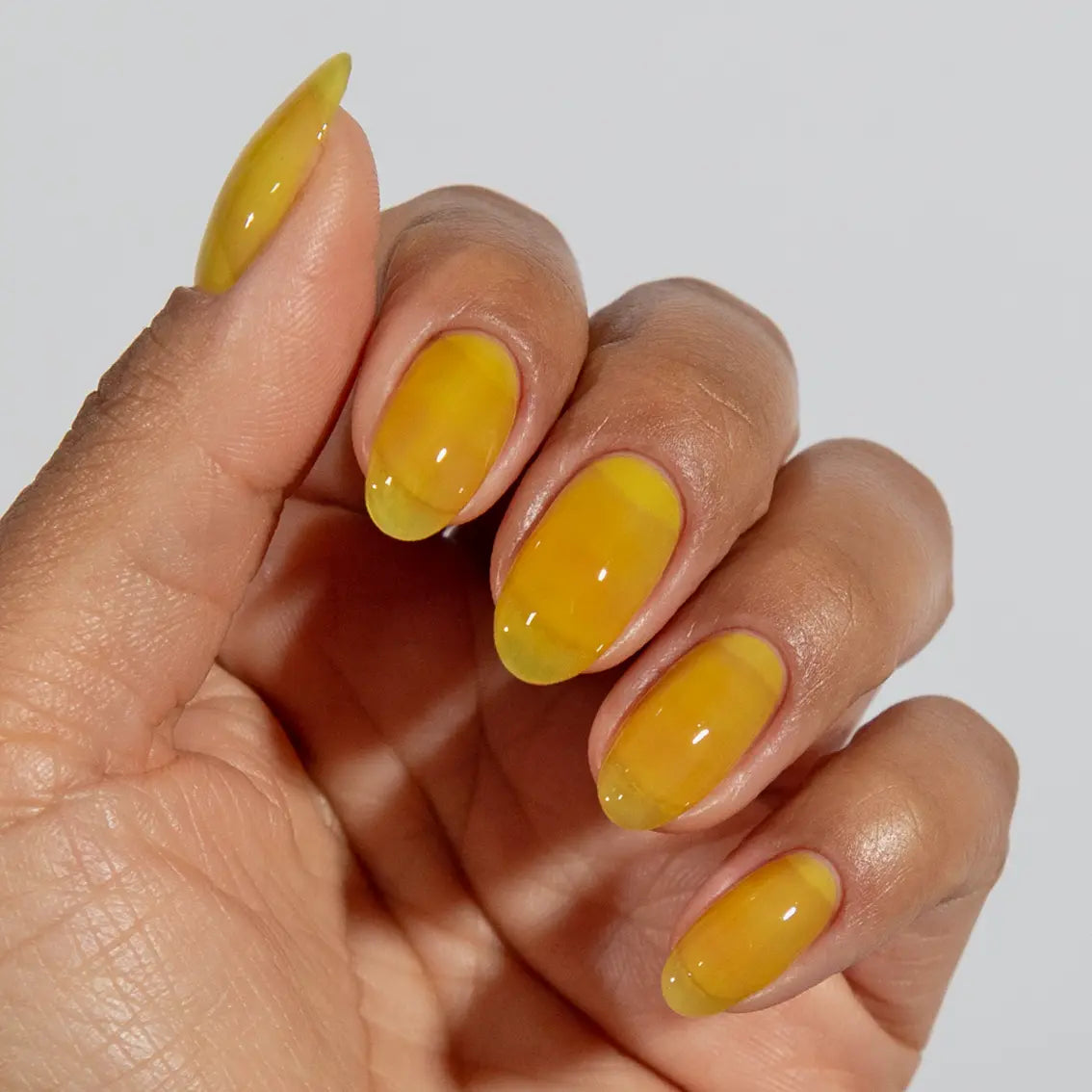 Hand with long almond nails wearing glossy DC Jelly Yuzu yellow jelly gel nail polish