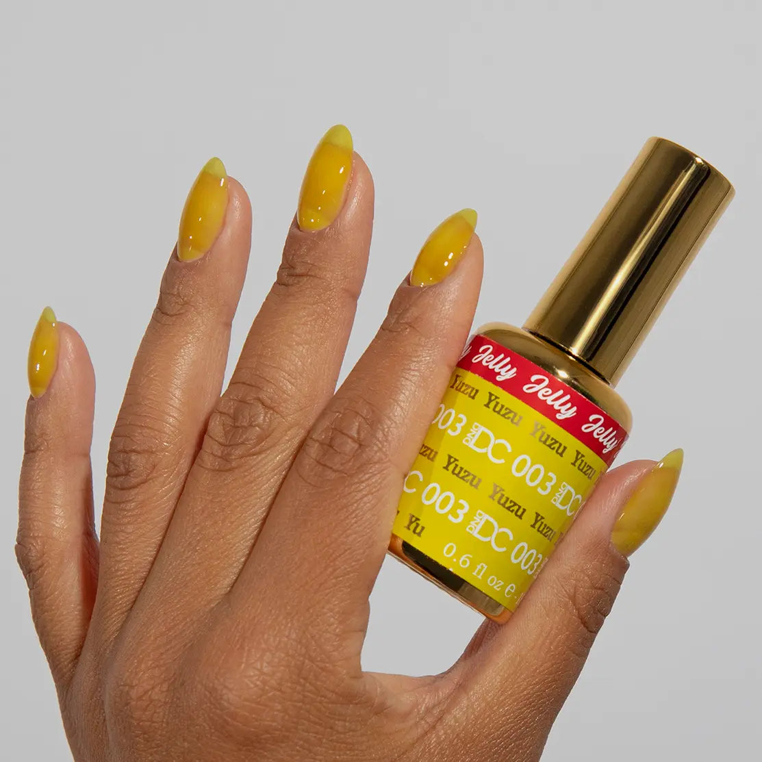 Hand with long almond nails wearing glossy DC Jelly Yuzu yellow jelly gel nail polish holding the bottle