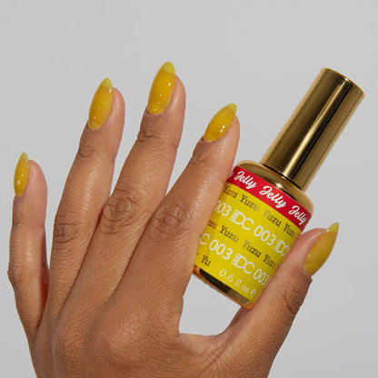 Hand with long almond nails wearing glossy DC Jelly Yuzu yellow jelly gel nail polish holding the bottle