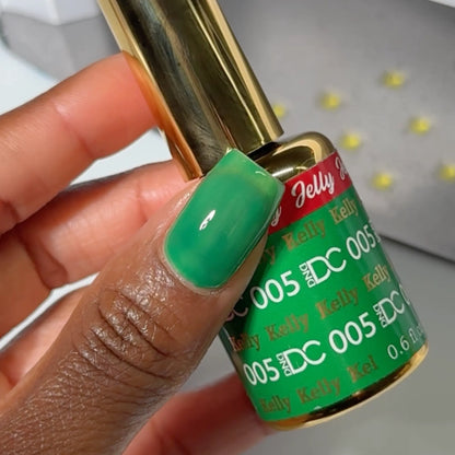 Close-up of a fingernail painted with DC Jelly Kelly emerald green jelly nail polish, holding a bottle of DND nail polish