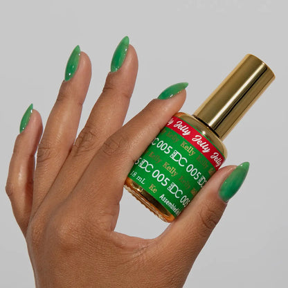 Hand with long almond-shaped nails wearing DC Jelly Kelly emerald green jelly nail polish, holding a bottle of DND nail polish