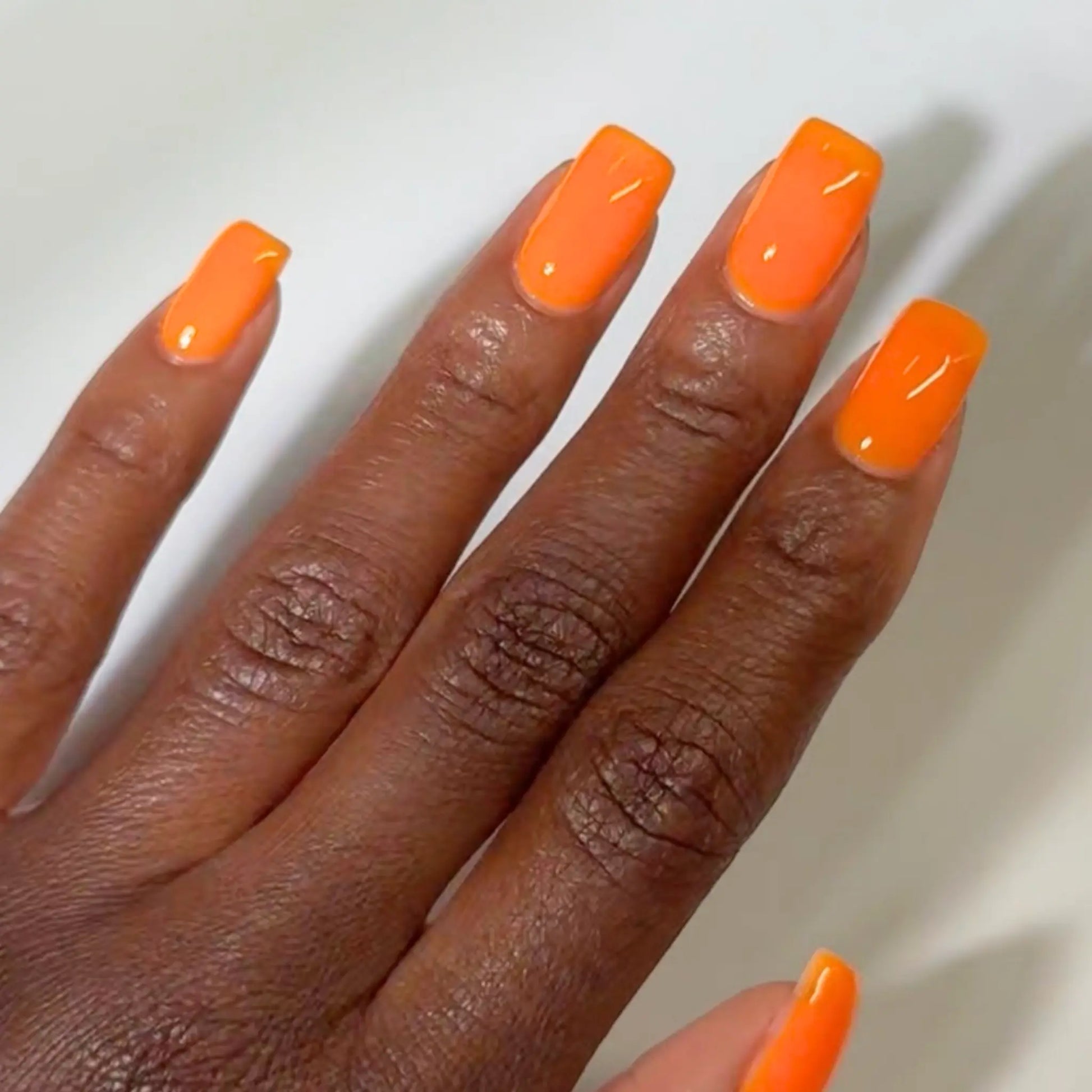 Close-up of a hand with long square-shaped nails wearing DC Jelly Orange true orange jelly nail polish