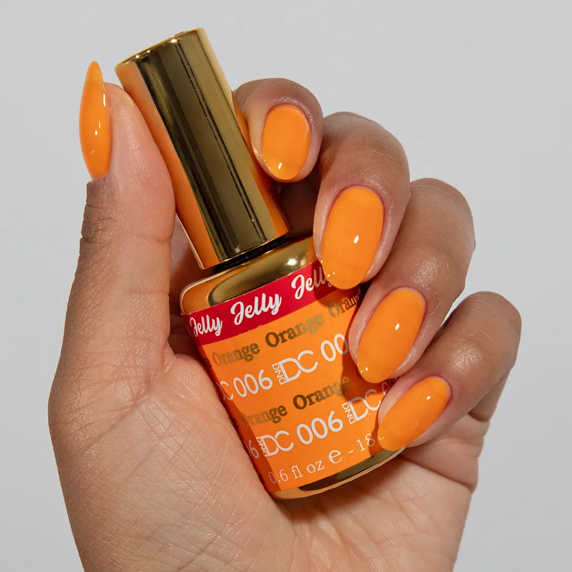 Hand with long almond-shaped nails wearing DC Jelly Orange true orange jelly nail polish, holding a bottle of DND nail polish