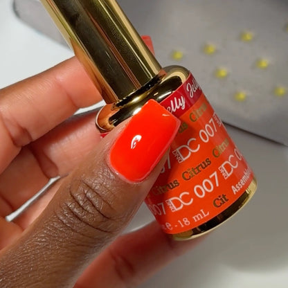 Hand with square-shaped nails wearing DC Jelly Citrus fiery orange jelly nail polish, holding a bottle of DND nail polish