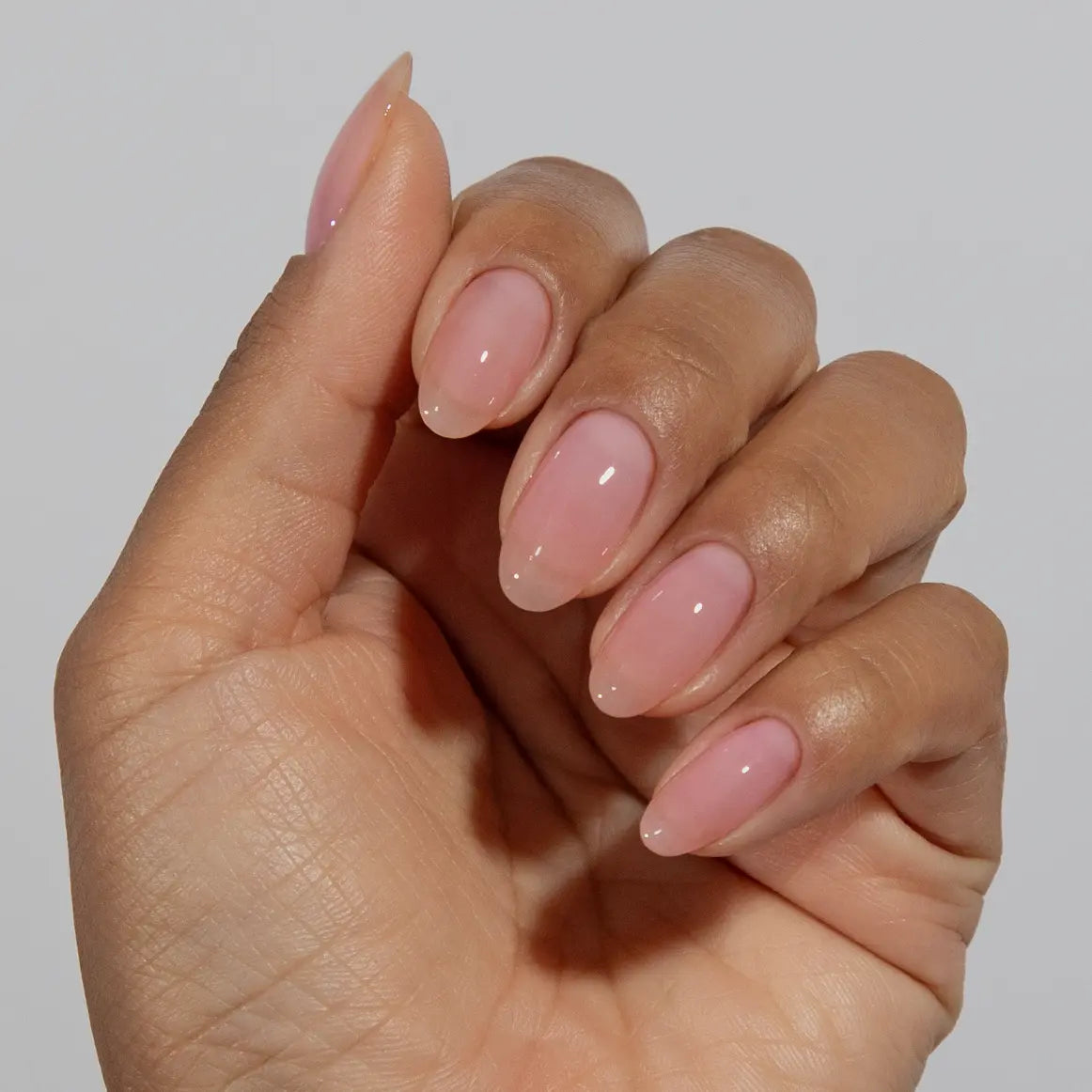 Close-up of a hand with long almond-shaped nails wearing DC Jelly Blush pale pink jelly nail polish