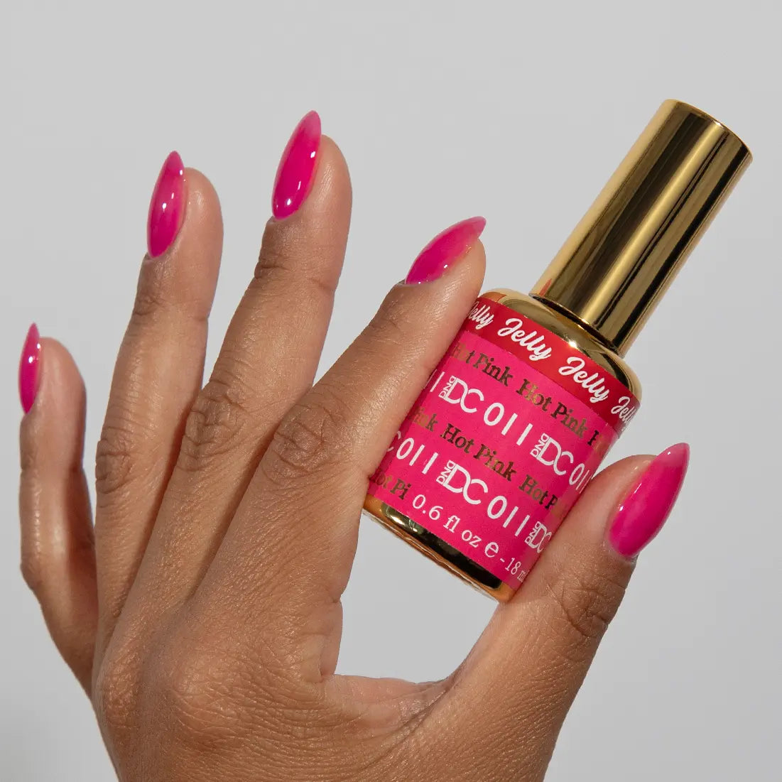Hand with hot pink jelly manicure holding a bottle of DC Jelly Hot Pink gel nail polish