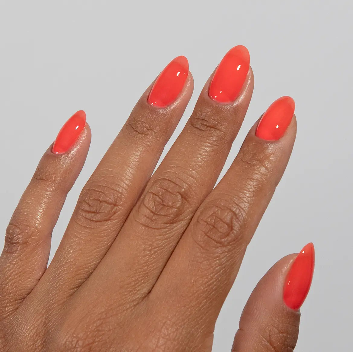 Hand with long almond nails wearing DC Jelly Poppy vibrant coral orange jelly nail polish
