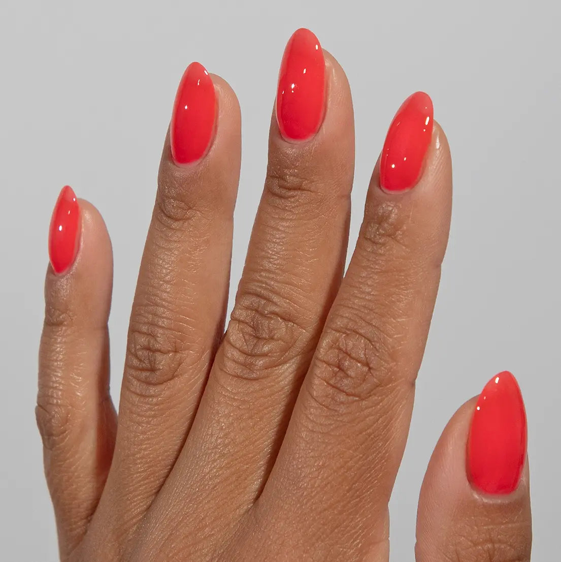 Hand with long almond nails wearing DC Jelly Tiger Blood bright coral-red jelly nail polish