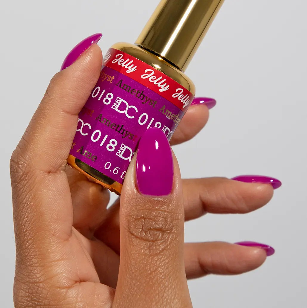 Hand with long almond nails wearing DC Jelly Amethyst vivid magenta-purple jelly nail polish, holding a bottle of DND nail polish