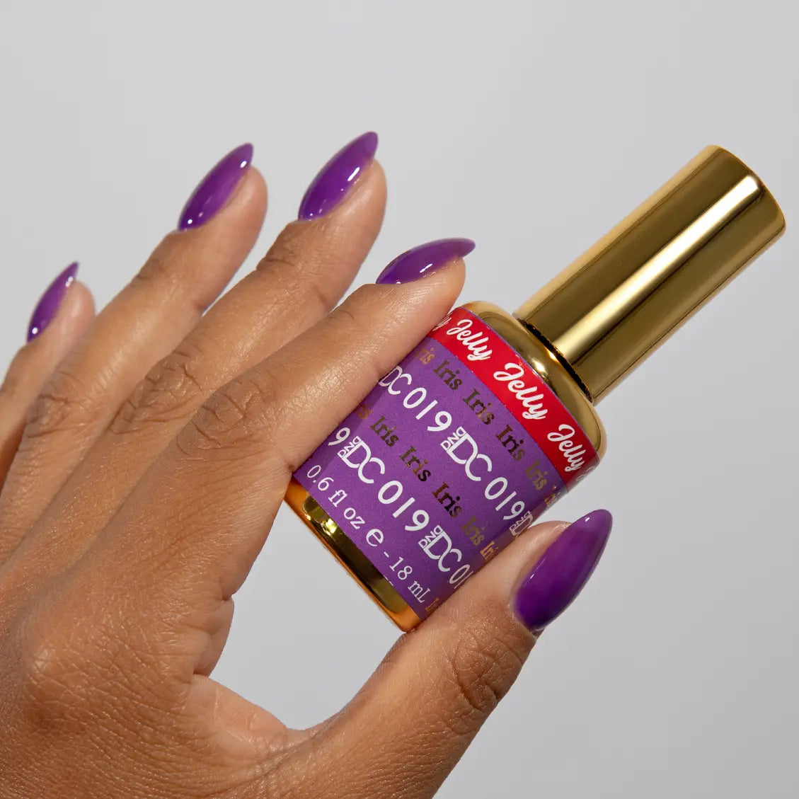 Hand with long almond nails wearing DC Jelly Iris deep purple jelly nail polish, holding a bottle of DND nail polish