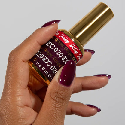 Hand with medium almond nails wearing DC Jelly Grape deep burgundy-purple jelly nail polish, holding a bottle of DND nail polish