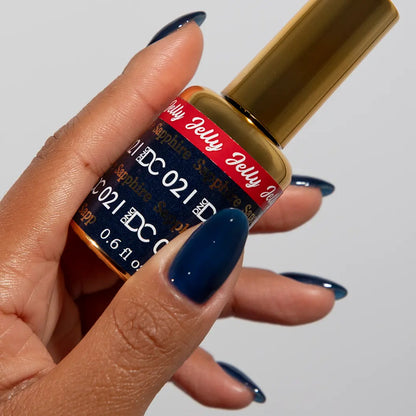 Hand with long almond nails wearing DC Jelly Sapphire deep sea blue jelly nail polish, holding a bottle of DND nail polish