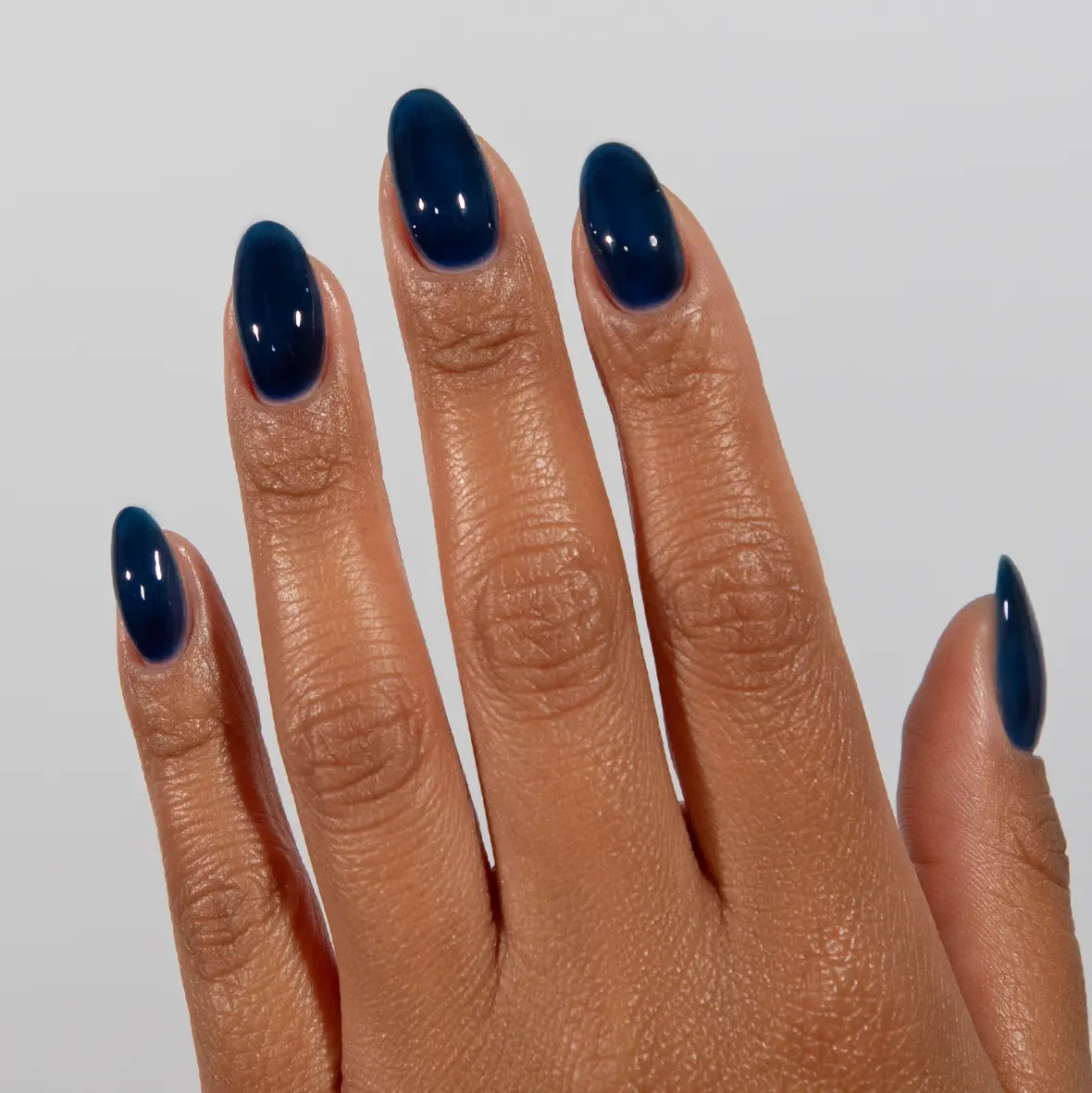 Hand with long almond nails wearing DC Jelly Sapphire deep sea blue jelly nail polish