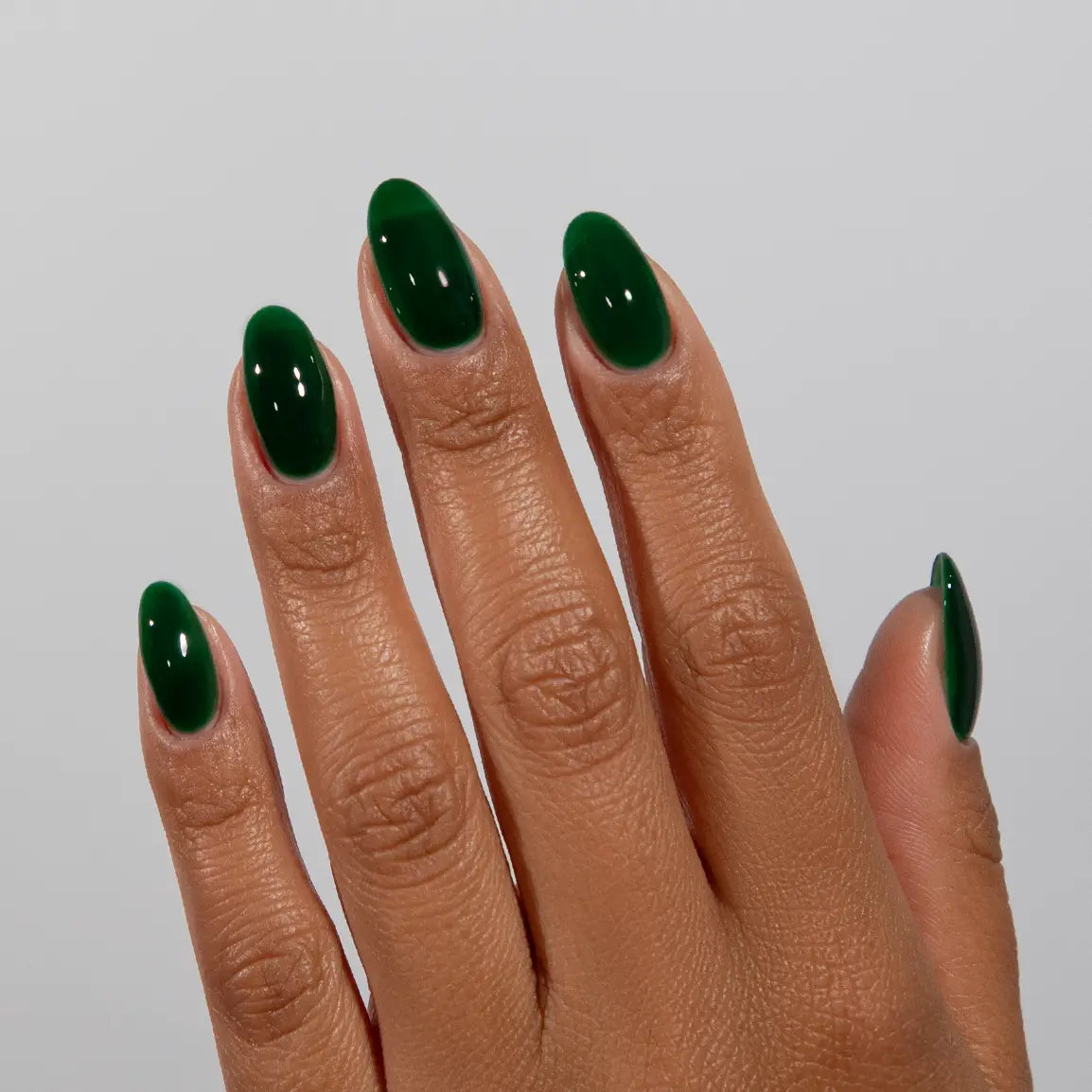 Hand with long almond nails wearing DC Jelly Emerald deep green jelly nail polish