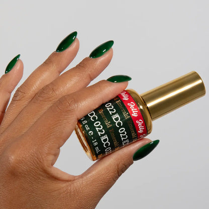 Hand with long almond nails wearing DC Jelly Emerald deep green jelly nail polish, holding a bottle of DND nail polish