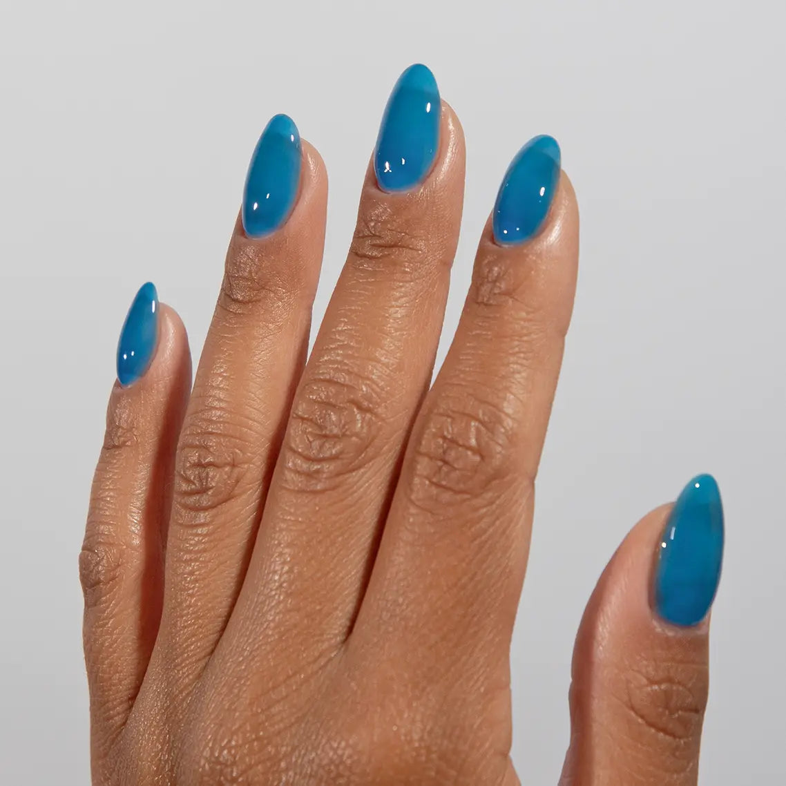 Hand with long almond nails wearing DC Jelly Capri bright azure blue jelly nail polish