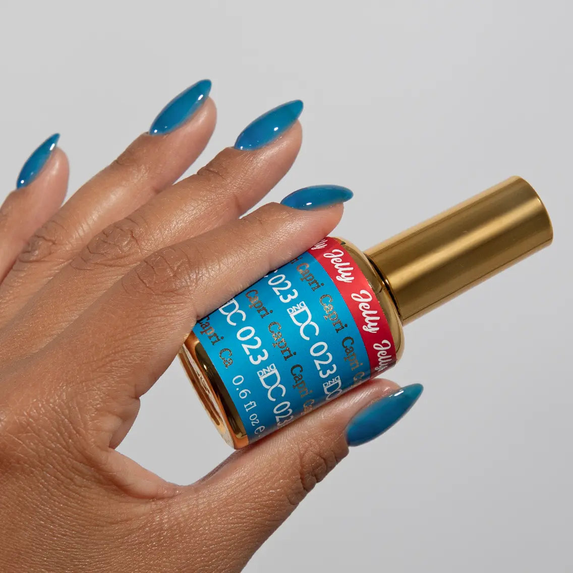 Hand with long almond nails wearing DC Jelly Capri bright azure blue jelly nail polish, holding a bottle of DND nail polish