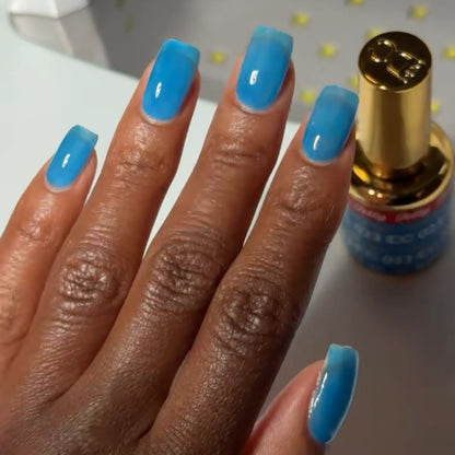 Hand with square nails wearing DC Jelly Capri bright azure blue jelly nail polish, next to a bottle of DND nail polish