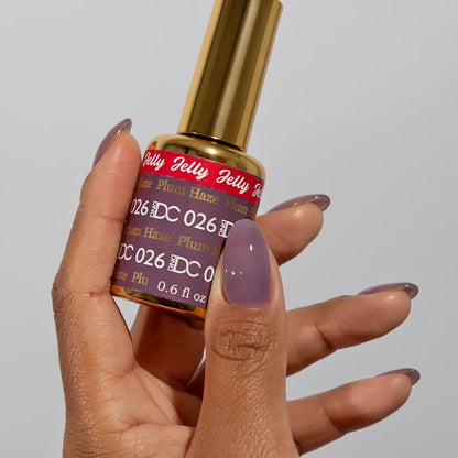 Hand with medium round nails wearing DC Jelly Plum Haze muted purple jelly nail polish, holding a bottle of DND nail polish