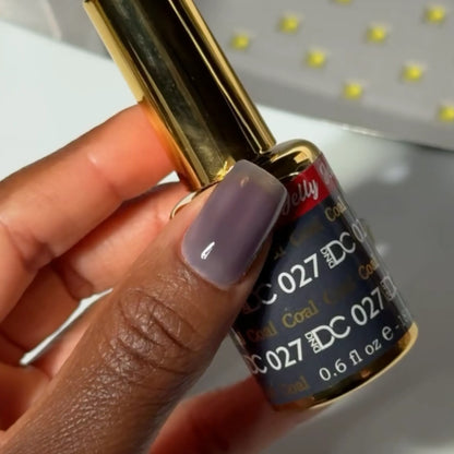 Finger with a square nail wearing DC Jelly Coal dark smoky grey jelly nail polish, holding a bottle of DND nail polish