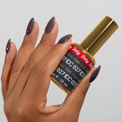 Hand with long almond nails wearing DC Jelly Coal dark smoky grey jelly nail polish, holding a bottle of DND nail polish