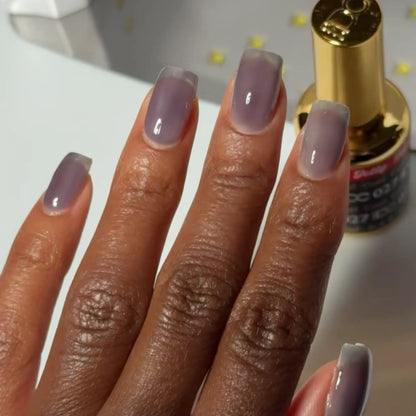 Hand with square nails wearing DC Jelly Coal dark smoky grey jelly nail polish, next to a bottle of DND nail polish