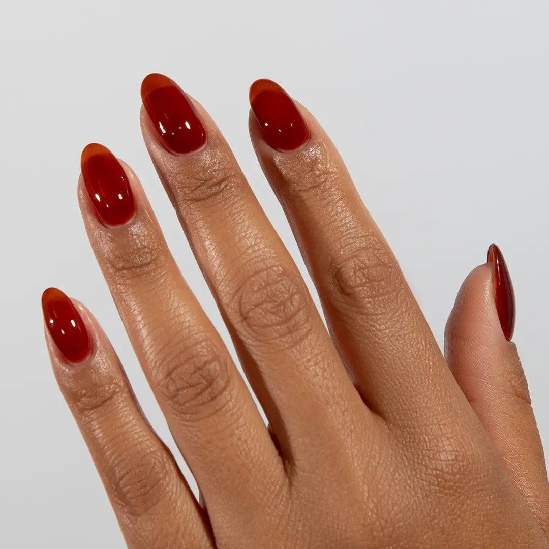 Hand with long almond nails wearing DC Jelly Amber deep amber brown-red jelly nail polish