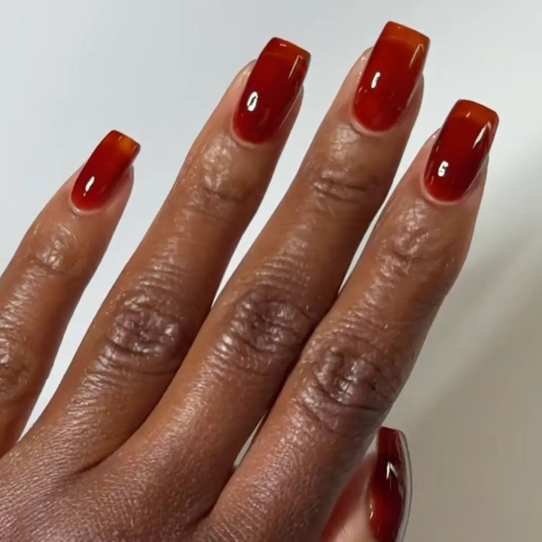 Hand with square nails wearing DC Jelly Amber golden brown translucent jelly nail polish
