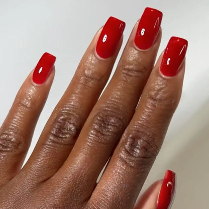 Hand with square nails wearing DC Jelly Sinners deep ruby red jelly nail polish with orange undertones
