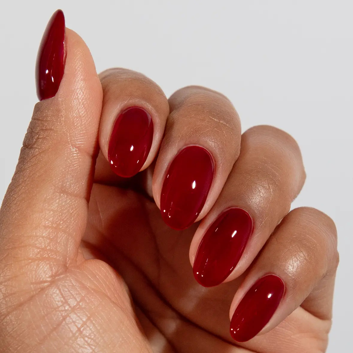 Hand with long almond nails wearing DC Jelly Sangria deep berry red jelly nail polish